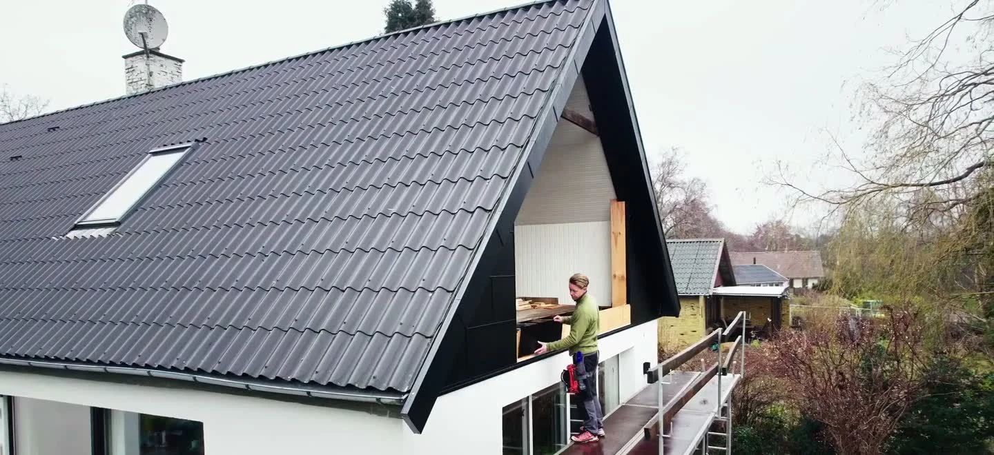 Tømrer i arbejde på stilladset ved gavlen af et hus med nyt sort tag